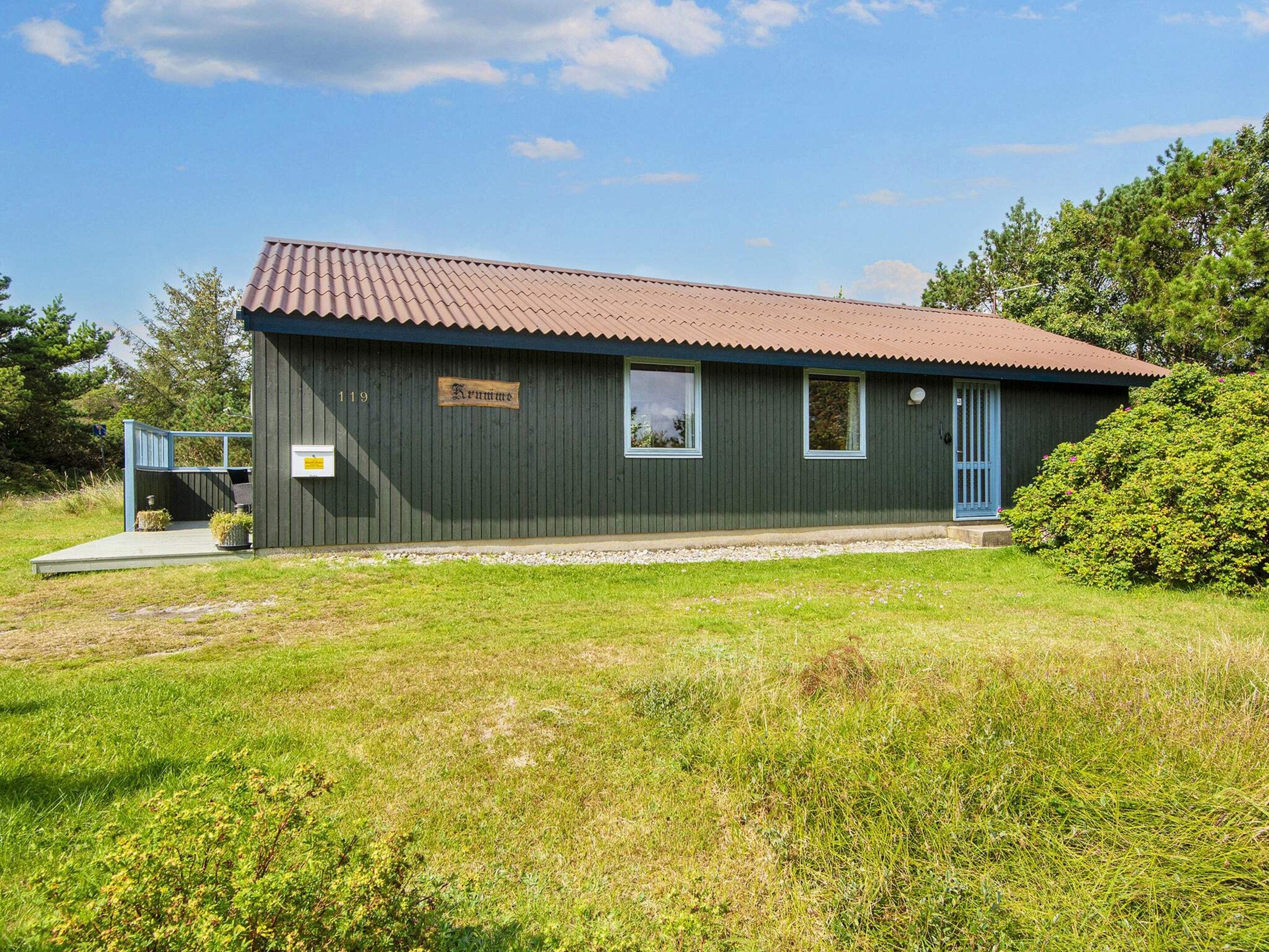Ein eingeschossiges Gebäude mit dunkler Fassade, rotem Ziegeldach und einer kleinen Veranda.
