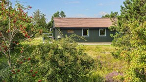 Un petit bâtiment vert foncé, surmonté d’un toit rouge, entouré d’une végétation luxuriante et d’arbres.