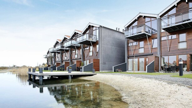 A modern residential building with multiple balconies, a reflective water body in front, and a gravel pathway. - Bright Apartment in Bogense Denmark With Terrace (Bogense)