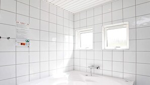 A modern bathroom with white tiles, a freestanding bathtub, and two wall-mounted windows. - 9 Person Holiday Home in Millinge (Millinge)