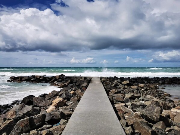 A concrete pathway leading to the sea, surrounded by large rocks.