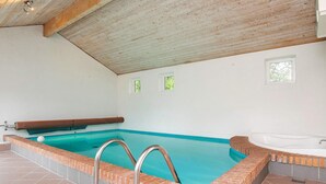 Ein Schwimmbecken mit Whirlpool, gefliestem Boden und einer Holzbalkendecke.