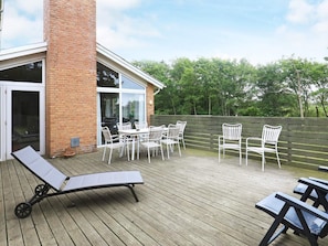 A wooden deck with a brick wall, a glass door, and white outdoor furniture. - 4 Star Holiday Home in Hjorring (Hjørring)