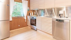 A modern kitchen with wooden cabinets, stainless steel appliances, and a window with white curtains.