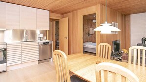 A compact, modern kitchen with wooden cabinets and a built-in dishwasher. A dining area with a wooden table and chairs is adjacent to the kitchen.
