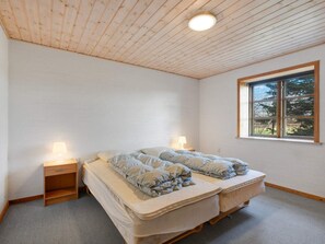 A room with a wooden ceiling, a bed with two pillows, a nightstand, a window with a view of trees, and a carpeted floor. - 12 Person Holiday Home in Nordborg (Nordborg)