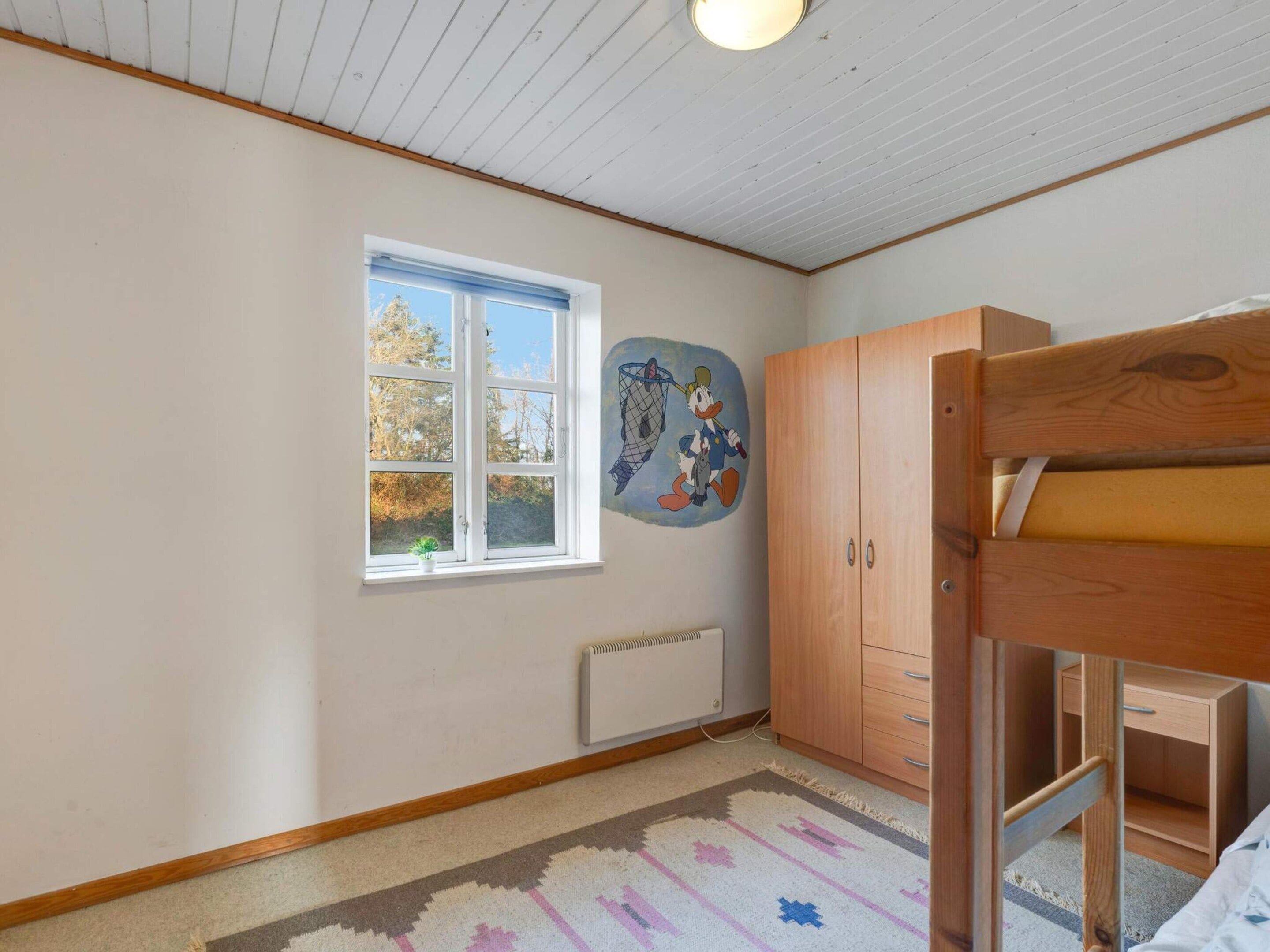 Een kamer met een stapelbed, een radiator, een raam met uitzicht op bomen, en een muur met een muurschildering van een stripfiguur.