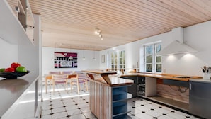 Une cuisine moderne avec un plafond en bois, un revêtement de sol en carreaux hexagonaux et un îlot central doté d’un évier.
