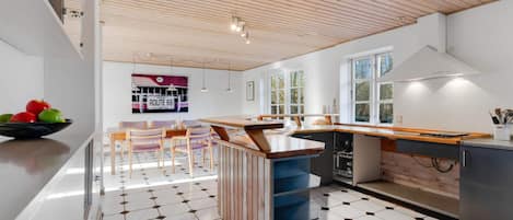 A modern kitchen with a wooden ceiling, a central island, and a black and white tiled floor.