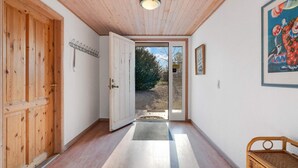 Un couloir avec un plancher et des murs en bois, une porte donnant sur l’extérieur et un tableau encadré accroché au mur.