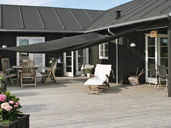 Eine überdachte Terrasse im Freien mit Holzmöbeln, einem weißen Liegestuhl und einem Blumentopf.