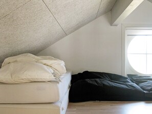 A room with a sloped ceiling, a bed with white and black bedding, and a window with a view.