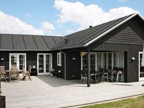 Ein schwarzes Gebäude mit geneigtem Dach, großen Fenstern und einer Terrasse mit Gartenmöbeln.