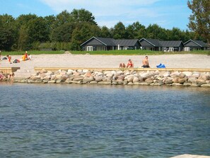 A lakeside resort with multiple cabins, a sandy beach, and a rocky shoreline. - 5 Star Holiday Home in Nysted (Nysted)