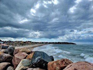 Una costa rocosa con olas, un cielo nublado y una costa distante con edificios.