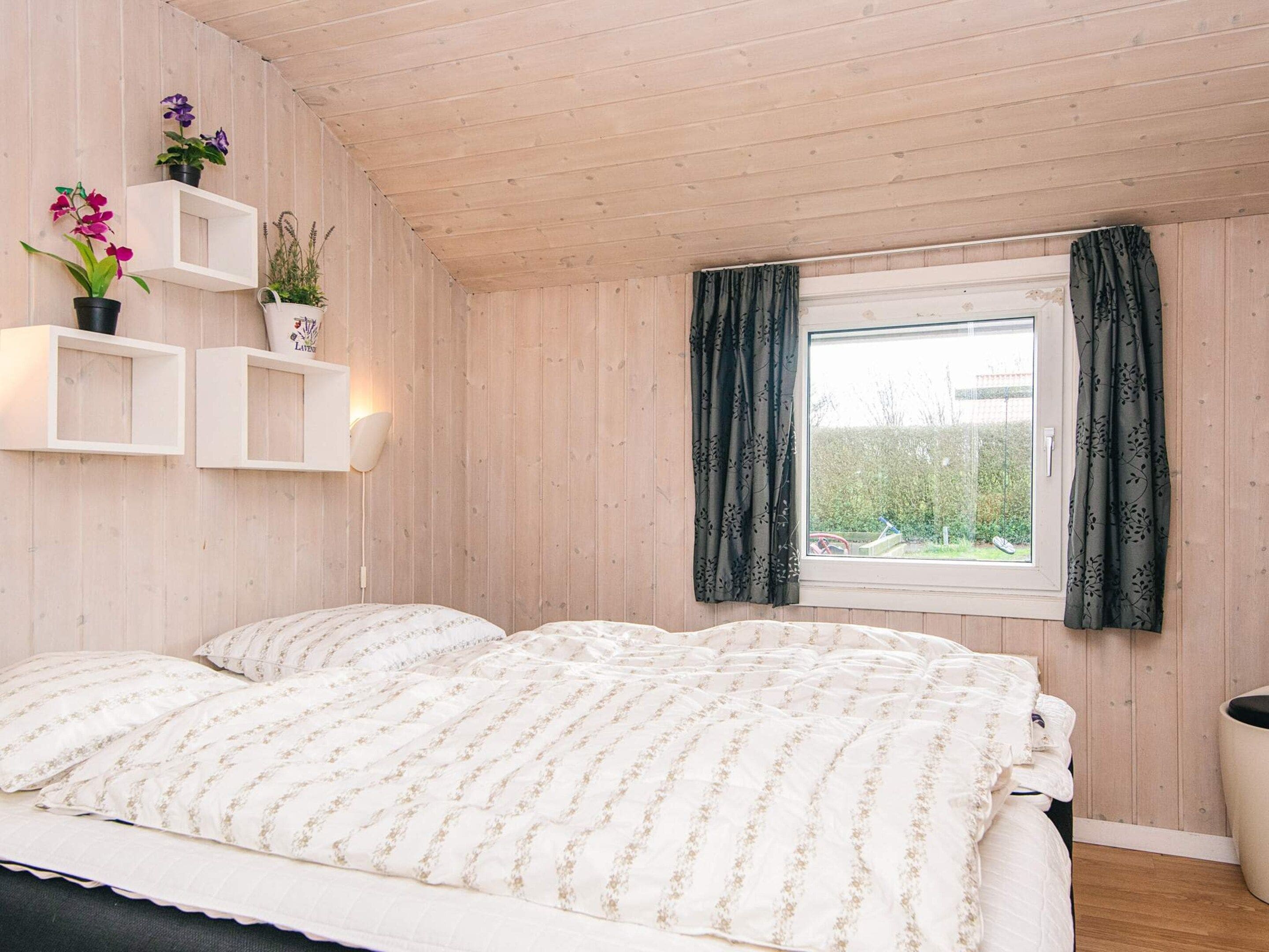 A bedroom with a bed, a window with curtains, and wall-mounted shelves with plants.