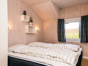 A room with a bed, wooden walls, a window with curtains, and wall-mounted shelves with plants. - 4 Star Holiday Home in Nordborg (Nordborg)