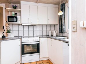 A kitchen with white cabinets, a microwave, a stove, and a sink. - 4 Star Holiday Home in Nordborg (Nordborg)