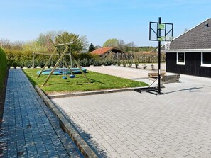 Une aire de jeux avec des balançoires et un panier de basket, un chemin pavé et un bâtiment avec une enseigne.