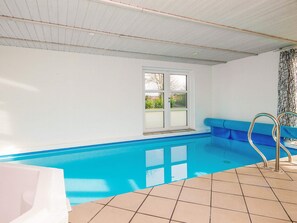 Une piscine avec un sol carrelé et une fenêtre donnant sur un paysage verdoyant.