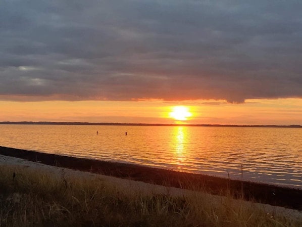 A sunset over a body of water with a distant shoreline and overcast sky.