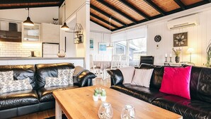 Ein modernes Wohnzimmer mit Holztisch, Ledersofas und einem Essbereich mit weißen Stühlen.
