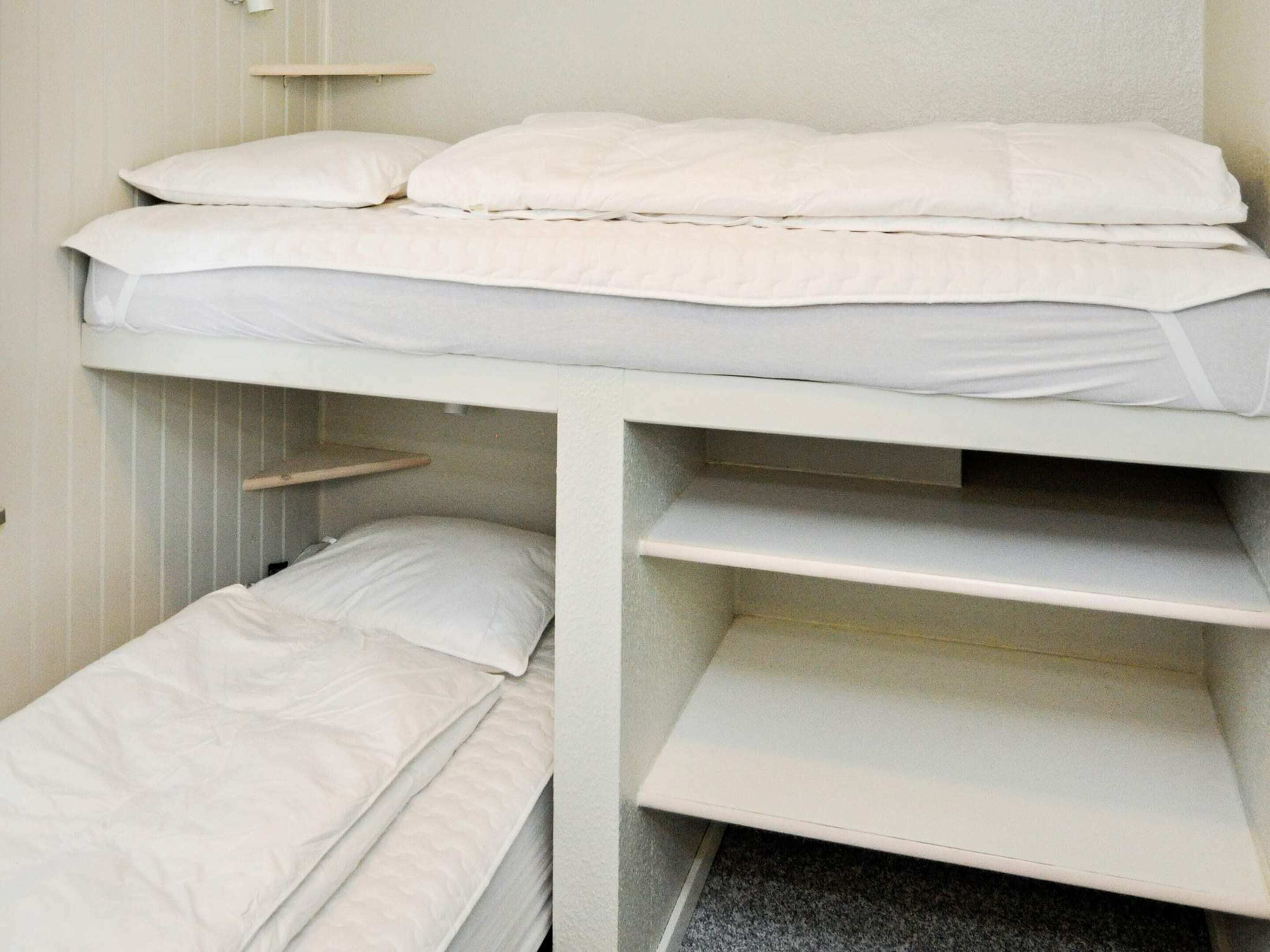 A bunk bed with two levels, each with a mattress and pillows. There are shelves built into the bed structure, and a small shelf above the lower bunk.