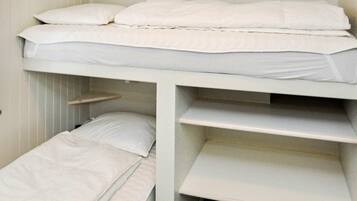 A bunk bed with two levels, each with a mattress and pillows. There are shelves built into the bed structure, and a small shelf above the lower bunk.
