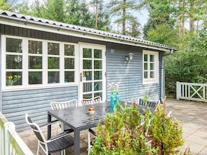 Edifici blau amb una zona de pati que inclou una taula i cadires, una tanca blanca i vegetació al fons.