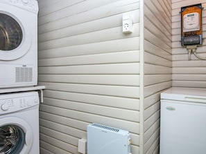 A laundry room with a stacked washer and dryer, a thermostat, and a power outlet.