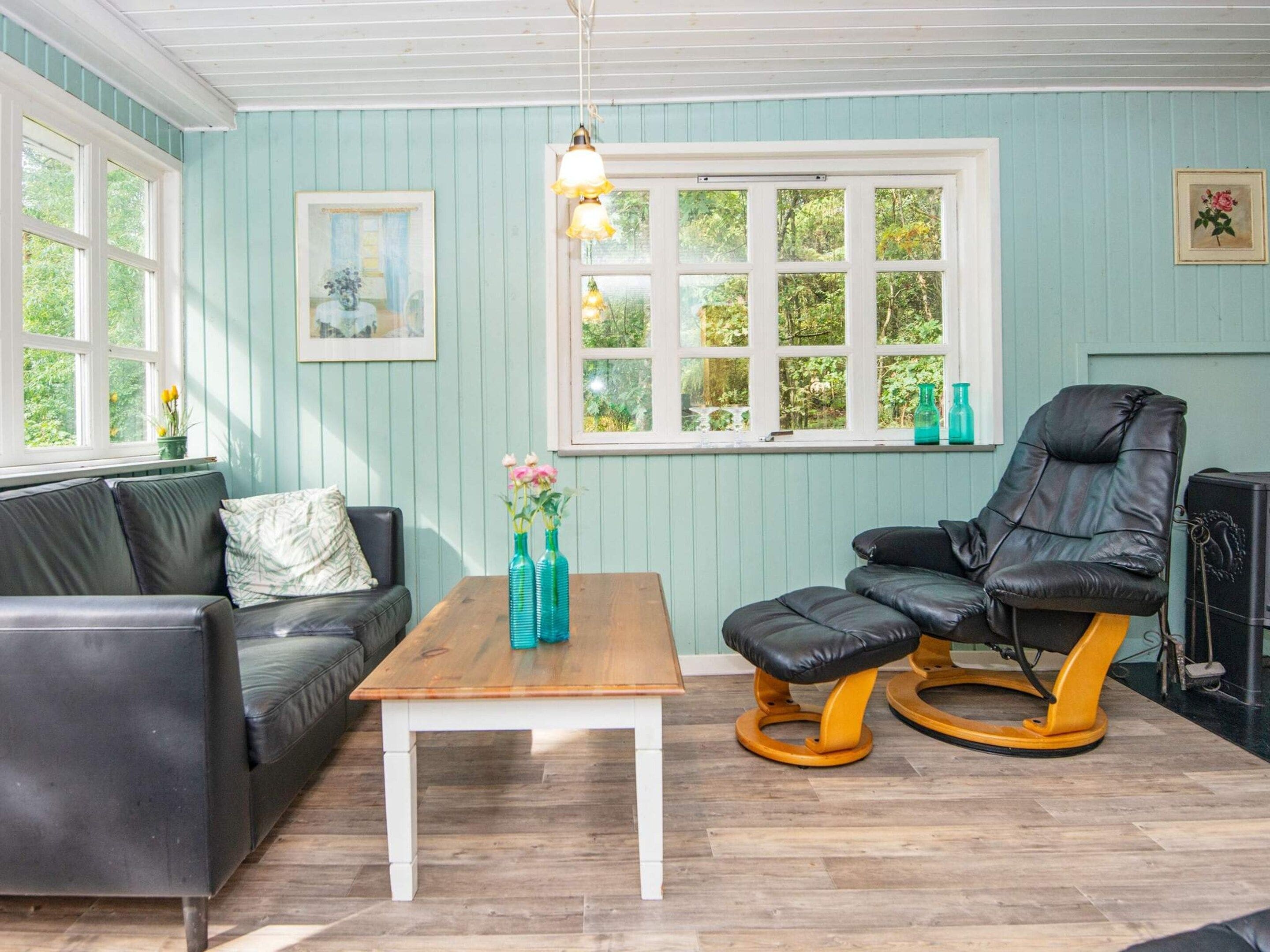 Una habitación con una mesa de madera, un sofá de cuero negro, una mecedora y una ventana con vista a zonas verdes.