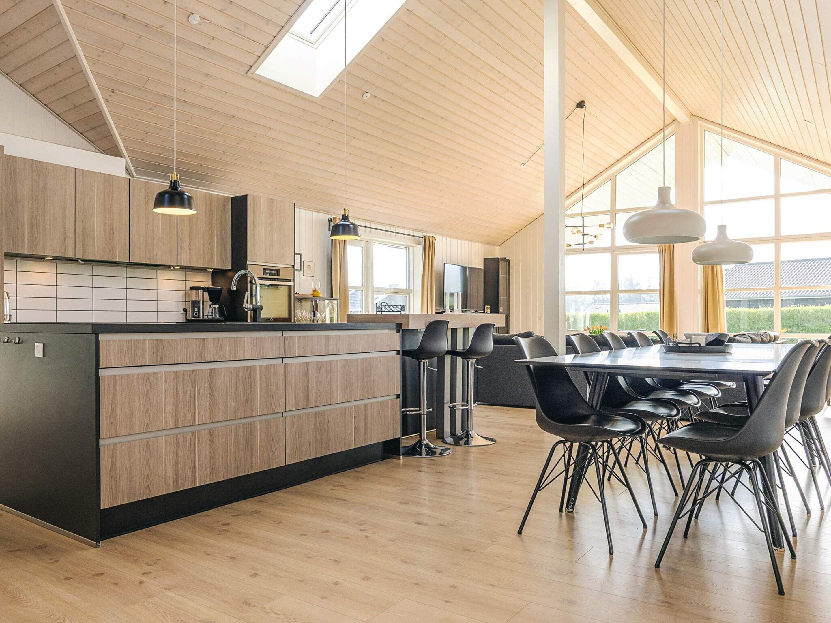 Una cocina moderna con armarios de madera, una isla central y un comedor con sillas negras.