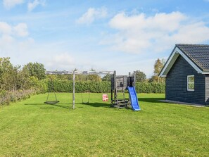A playground with a swing set and a slide, a small shed, and a house with a sloped roof. - 5 Star Holiday Home in Hadsund (Hadsund)