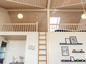 A loft-style room with a wooden ceiling, a loft bed, a ladder, and a view through a skylight.