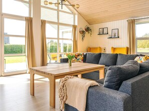 A modern living room with a wooden table, grey sofa, and large windows.