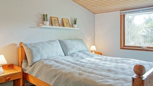 A bedroom with a wooden bed, a nightstand, a bedside table, a window, and a shelf with potted plants.