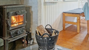 A stone fireplace with a visible fire, a wooden chair, and a metal bucket with logs.