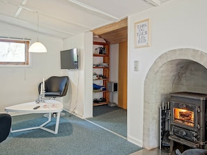 Ein gemütliches Zimmer mit Kamin, Fernseher, Bücherregal und bequemen Sesseln.