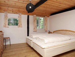 A bedroom with a wooden ceiling, a bed with white bedding, a wooden dresser, and two windows with floral curtains. - 12 Person Holiday Home in Laeso-by Traum (Læsø)