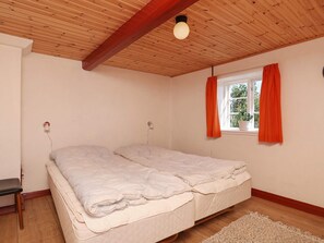 A bedroom with a wooden ceiling, a bed with a white mattress, a nightstand, a window with orange curtains, and a small potted plant on the windowsill. - 12 Person Holiday Home in Laeso-by Traum (Læsø)