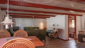 A cozy living room with a wooden dining table, wicker chairs, a sofa, and a television. - 12 Person Holiday Home in Laeso-by Traum (Læsø)
