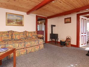 A cozy living room with a patterned sofa, a small table with a plate, a decorative stove, and a door leading to another room. - 12 Person Holiday Home in Laeso-by Traum (Læsø)