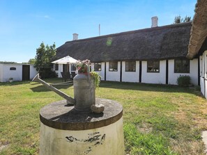 A thatched-roof building with a white exterior, a metal watering can on a post, and a small table with chairs in the foreground. - 12 Person Holiday Home in Laeso-by Traum (Læsø)