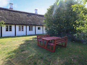 A thatched-roof building with a wooden bench and table in a grassy yard. - 12 Person Holiday Home in Laeso-by Traum (Læsø)