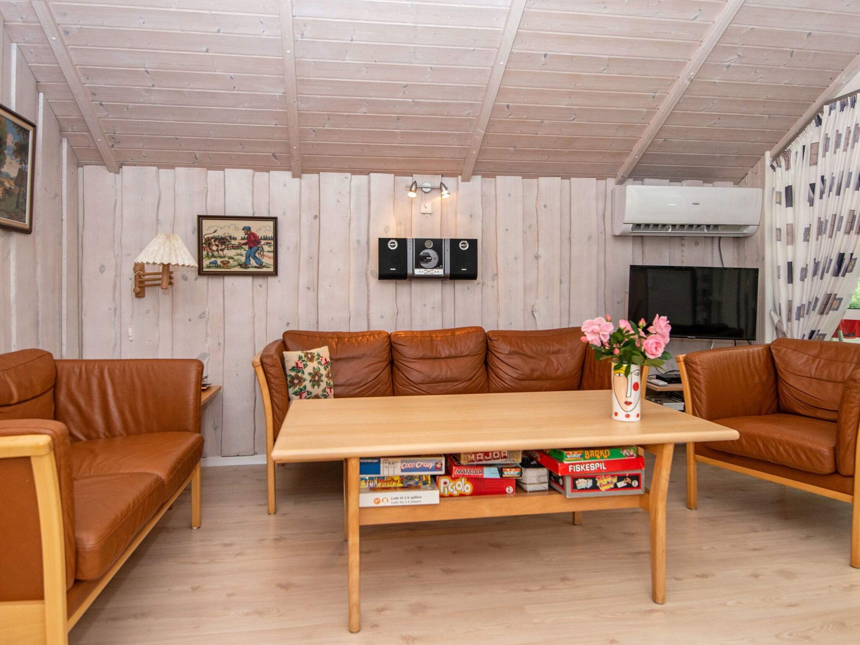 A living room with a wooden ceiling, a brown leather sofa, a wooden coffee table with board games, a television, and a framed picture on the wall.