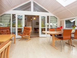 A spacious room with a high ceiling, large windows, and a dining area with wooden furniture.