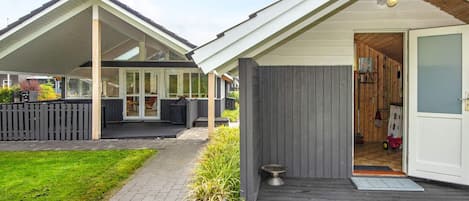 A modern house with a covered patio, a wooden deck, and a grassy yard.