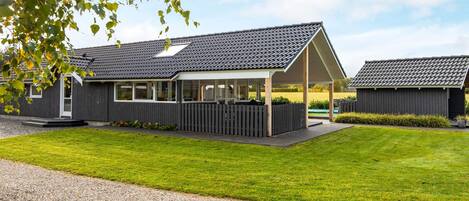 A modern building with a covered patio area, a gravel driveway, and a well-maintained lawn.