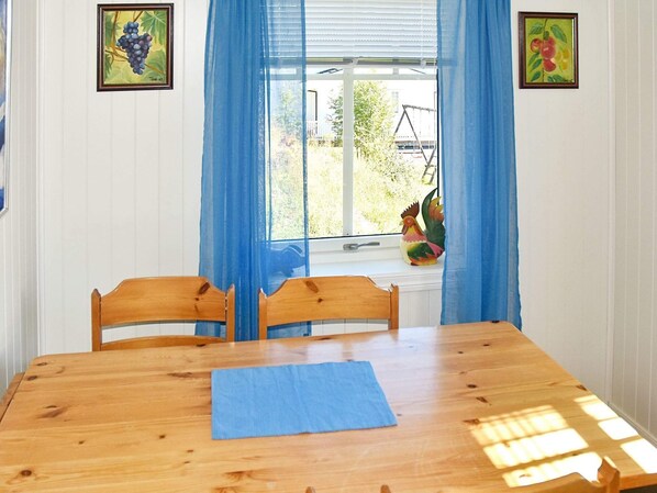 A dining room with a wooden table, chairs, a blue table runner, and a window with blue curtains. - 4 Star Holiday Home in Oksvoll (Orland)