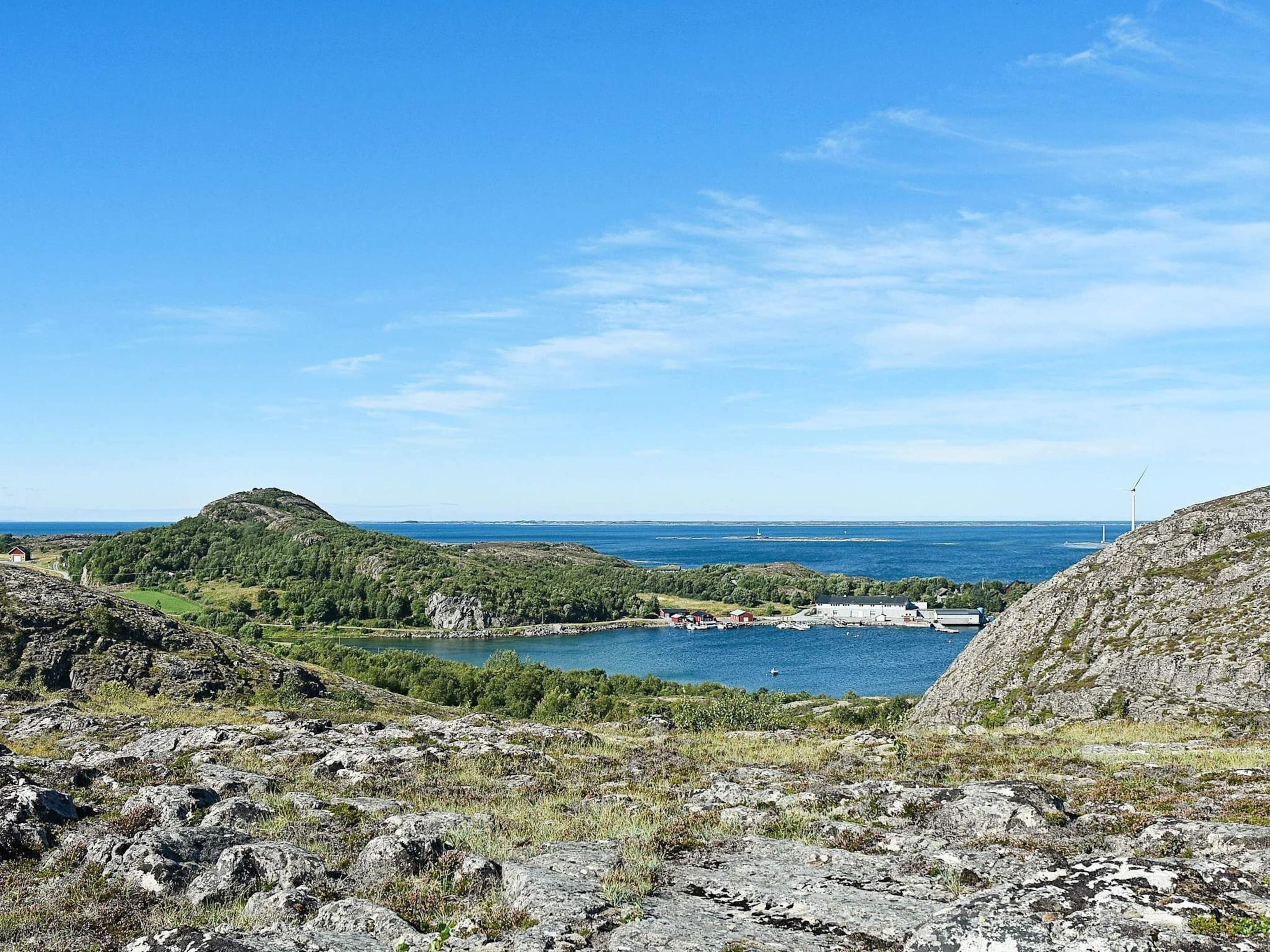 A coastal landscape with rocky terrain, a small body of water, and distant wind turbines.